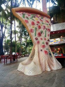 Un immense morceau de pizza a été spécialement conçu pour apporter une touche décorative et publicitaire au restaurant. Il est fabriqué en résine et en fibre de verre, et agrémenté d'une finition artistique à la peinture.