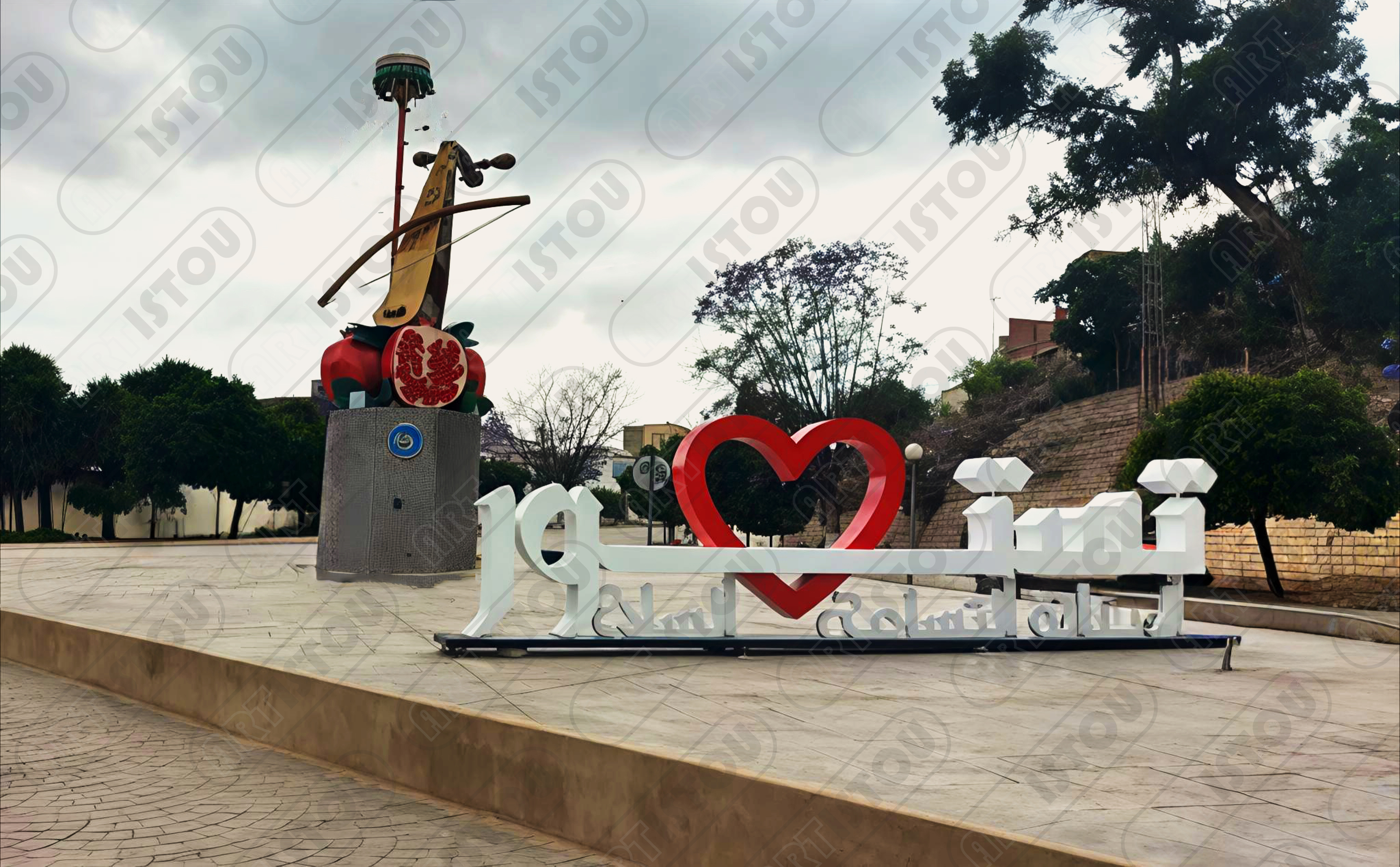 Photo panoramique du nouveau monument emblématique de Testour (Tunisie), affichant le mot "Testour" avec un grand cœur rouge. À gauche, une sculpture représentant un instrument de musique (comme un violon ou un rebab) posé sur une grenade. Ce lieu reflète la culture andalouse et le patrimoine historique de la ville. Idéal pour les guides de voyage ou les articles sur le tourisme en Tunisie.